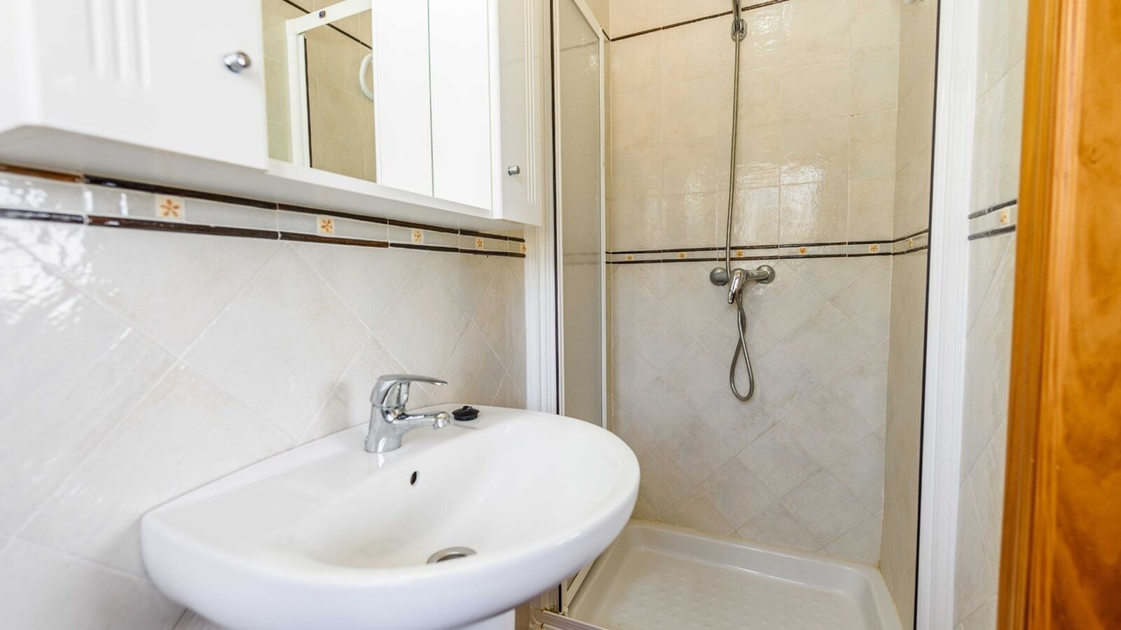 A bathroom with a white sink, a mirror above it, and a shower area with tiled walls.