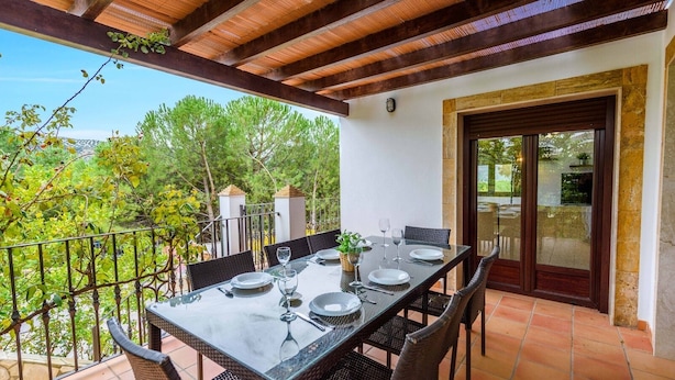 Un coin repas avec une table dressée pour quatre personnes, entourée de chaises en osier, sous une pergola en bois.