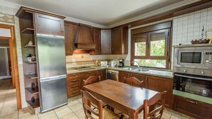 Une cuisine avec des meubles en bois, un réfrigérateur en acier inoxydable, une table à manger en bois et un four encastré.