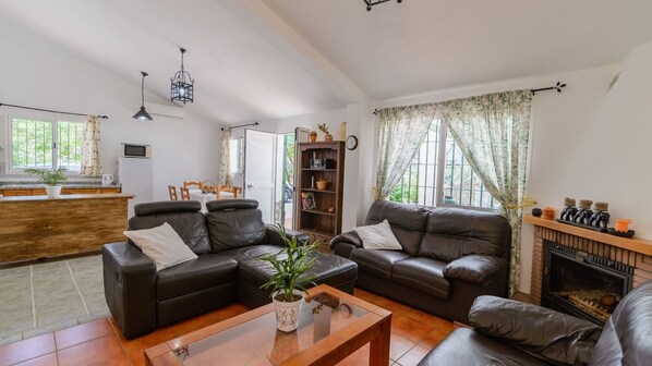 A spacious living room with leather sofas, a coffee table, a fireplace, and a kitchen area in the background. - Casa Lirios Cómpeta by Ruralidays (Málaga)