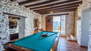 Una mesa de billar en una habitación rústica con paredes de piedra, vigas de madera y vistas a las montañas.