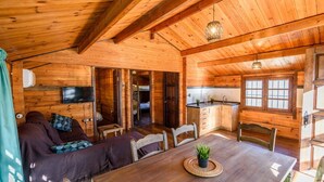 Ein gemütliches Blockhaus-Interieur mit einem Holztisch, einer Couch, einem an der Wand montierten Fernseher und einer Küchenzeile.