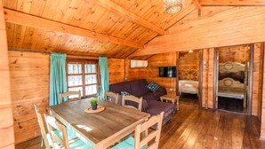 Ein Holzblockbau-Innenraum mit Esstisch, zwei Sofas, Fernseher und einem Bett.