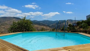 Ein rechteckiger Pool mit Holzdeckrändern, Metallleitern und einer Bergkulisse.
