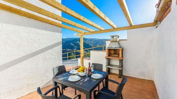 A patio with a table set for two, a brick oven, and a view of mountains.