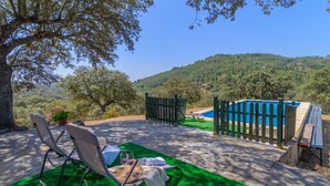 A poolside area with a view of a hillside, a wooden fence, and a table with a chair and a bottle. - El Cortijo de Camama Villaviciosa de Córdoba by Ruralidays (Córdoba)