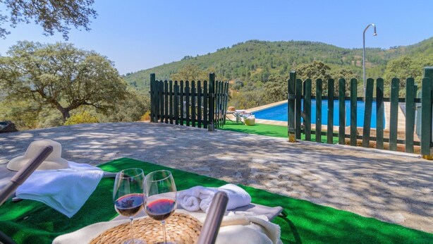 A poolside area with a view of a mountain and a pool. There are lounge chairs, a hat, and two glasses of red wine on a green mat. - El Cortijo de Camama Villaviciosa de Córdoba by Ruralidays (Córdoba)