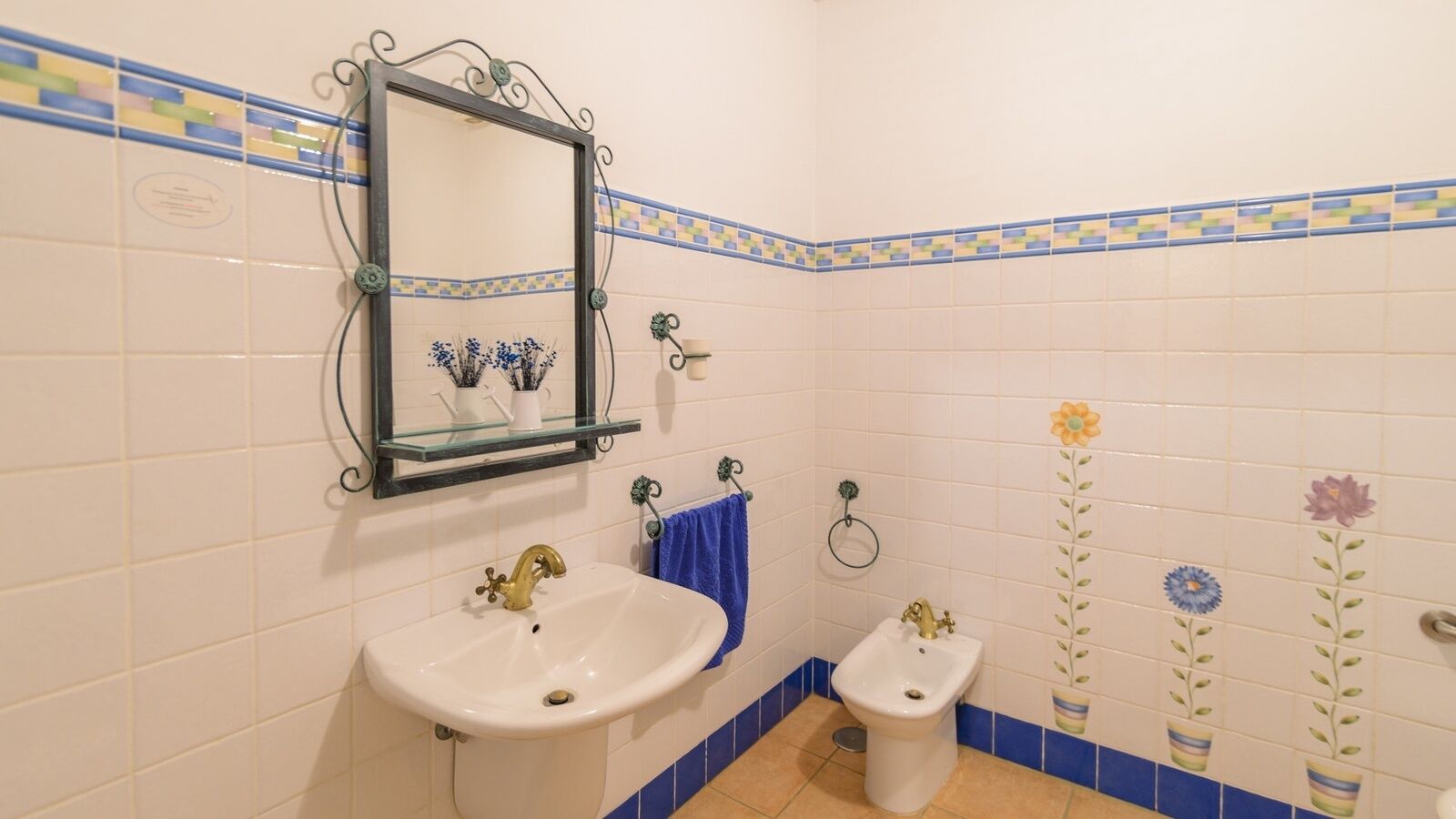 Une salle de bain avec un lavabo blanc, un bidet et un miroir surmonté d’une étagère en verre.