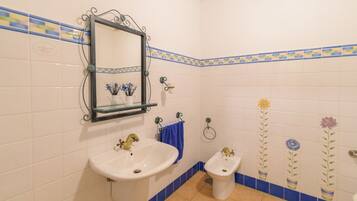 Une salle de bain avec un lavabo blanc, un bidet et un miroir surmonté d’une étagère en verre.