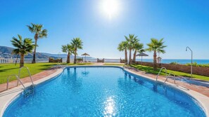 A swimming pool with clear blue water, surrounded by palm trees and a white fence, with a view of the ocean and mountains in the background. - Adosadas Lambda Deluxe Almuñécar by Ruralidays (Granada)