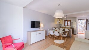 A modern living room with a red chair, a TV, a dining area with chairs, and a kitchen with a fridge. - Adosadas Lambda Deluxe Almuñécar by Ruralidays (Granada)