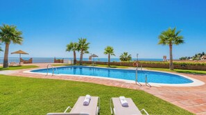 A swimming pool with a clear view of the sea, surrounded by palm trees and a grassy area with lounge chairs. - Adosadas Lambda Deluxe Almuñécar by Ruralidays (Granada)