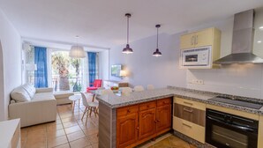 A modern kitchen with granite countertops, wooden cabinets, and stainless steel appliances. There is a dining area with a table and chairs, and a living room with a sofa and a TV. - Adosadas Lambda Deluxe Almuñécar by Ruralidays (Granada)