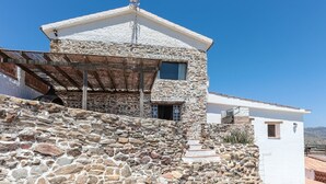 Un edificio de piedra con techo inclinado, una pérgola de madera y un ventanal pequeño.