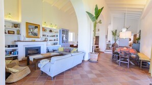 A spacious living room with a fireplace, a sofa, a dining area with a table and chairs, and a large plant. - Finca Las Encinillas Arcos de la Frontera by Ruralidays (Cádiz)