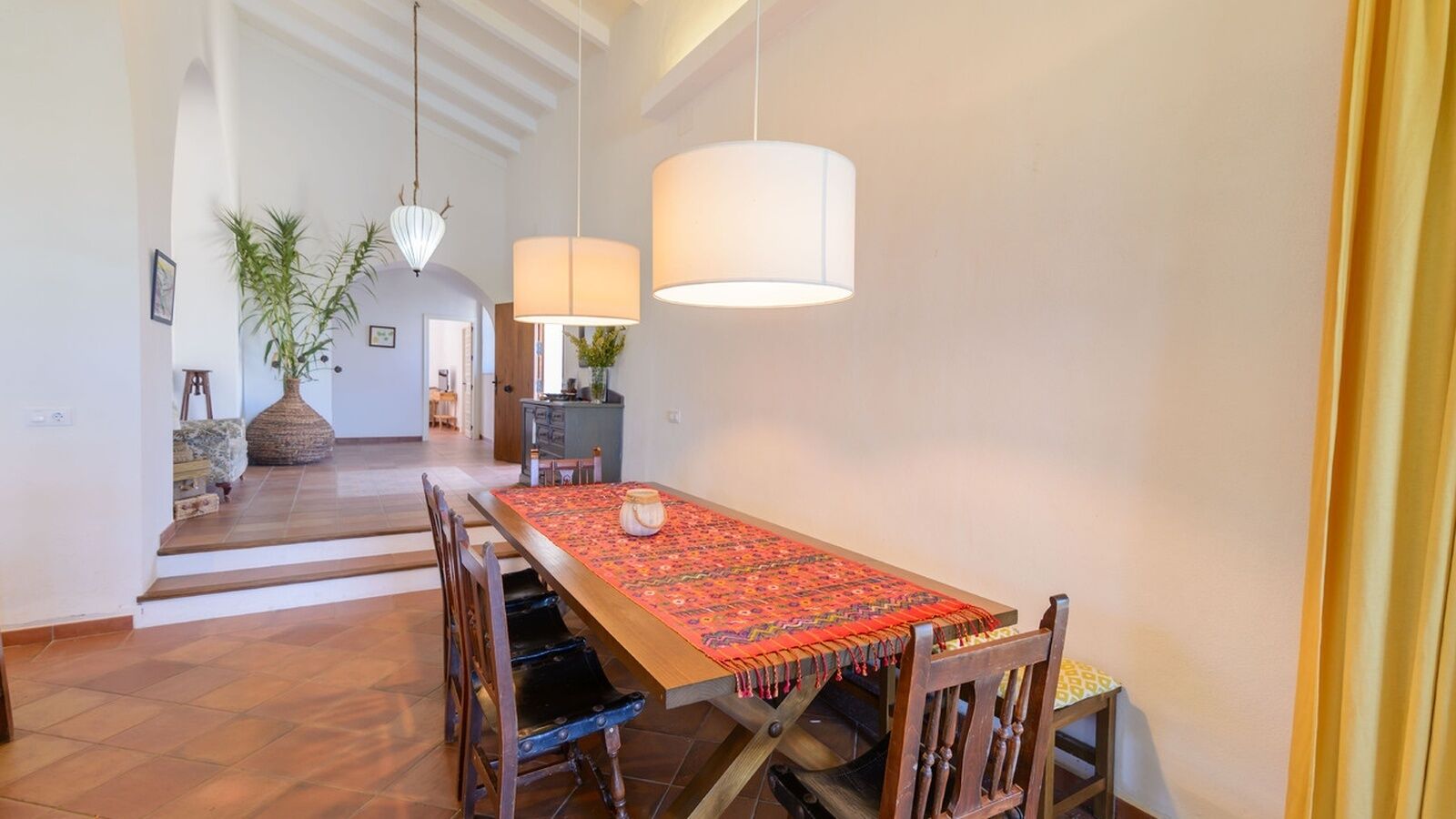 Un espace repas avec une longue table en bois, des chaises et des lampes suspendues.