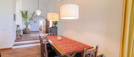 Un espace repas avec une longue table en bois, des chaises et des lampes suspendues.