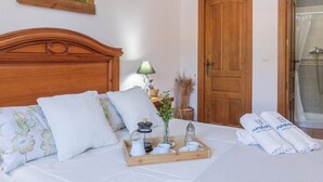 Een opgemaakt bed met bloemenkussens, een dienblad met theeservies en handdoeken met branding.