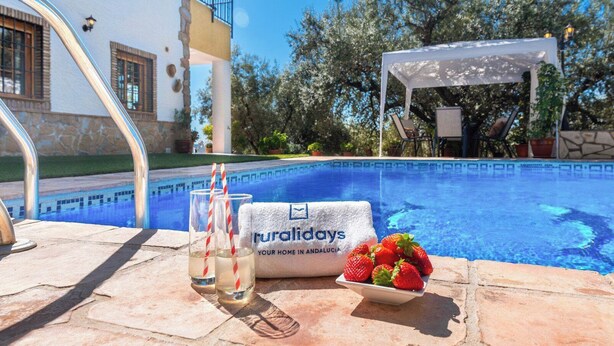 Een zwembadterras met een handdoek, glazen en aardbeien, en een bordje met de tekst 'ruraldays your home in Andalusia'.