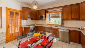 A kitchen with wooden cabinets, a glass dining table with red cushions, and a stainless steel dishwasher. - Torreón de Morayma Baena by Ruralidays (Córdoba)