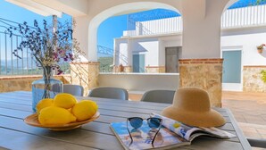 A table with a bowl of lemons, a straw hat, and sunglasses on a wooden table with a view of a building and a balcony. - Torreón de Morayma Baena by Ruralidays (Córdoba)