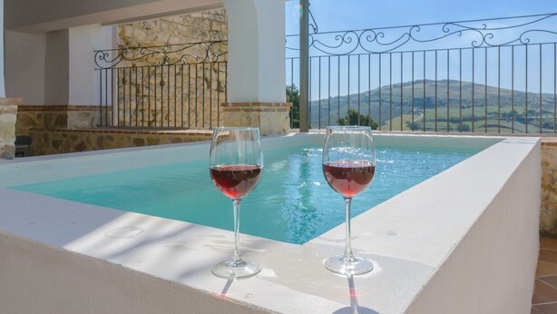 A poolside area with two glasses of red wine, a stone wall, and a view of hills in the background. - Torreón de Morayma Baena by Ruralidays (Córdoba)