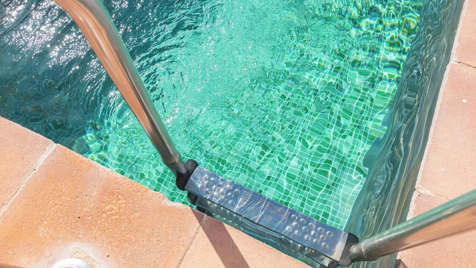 Une piscine aux eaux claires, bordée de carreaux et dotée d’un escalier en métal.