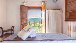 A bedroom with a bed, a wooden chair, a window with a view of mountains, and a pair of towels on the bed. - Guajar 2 Monda by Ruralidays (Málaga)