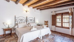 A bedroom with two beds, a wooden ceiling, a window with wooden shutters, and patterned floor tiles. - Guajar 2 Monda by Ruralidays (Málaga)