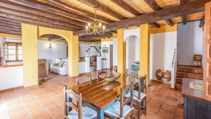 A spacious dining area with a wooden table and chairs, a chandelier, and a kitchen area in the background. - Guajar 2 Monda by Ruralidays (Málaga)