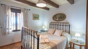 A bedroom with a bed, a nightstand, a lamp, a painting, and a window with curtains.
