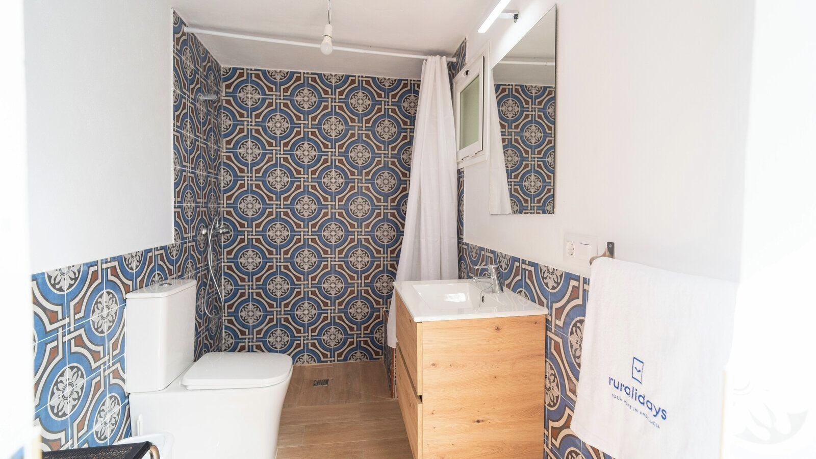 A bathroom with patterned tiles, a white toilet, a wooden vanity, and a shower curtain.