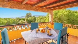 Una terraza con una mesa dispuesta para el desayuno, pilares de piedra y vistas a zonas verdes y montañas.