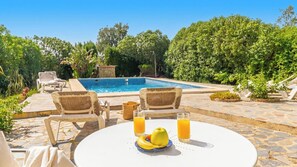A poolside area with a table, chairs, and a fruit bowl.