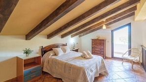 Un dormitorio con cama, vigas de madera, cómoda, silla y ventana.