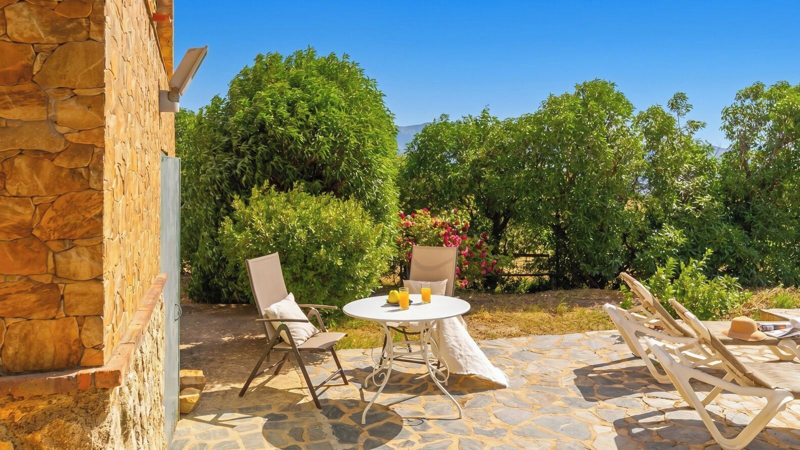 Une terrasse extérieure avec un sol en pierre, une table ronde, deux chaises et une vue sur une végétation luxuriante et des arbres.