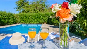 A poolside setting with a glass of orange juice, a white hat, and a vase with flowers. - Casita Monica Órgiva by Ruralidays (Granada)