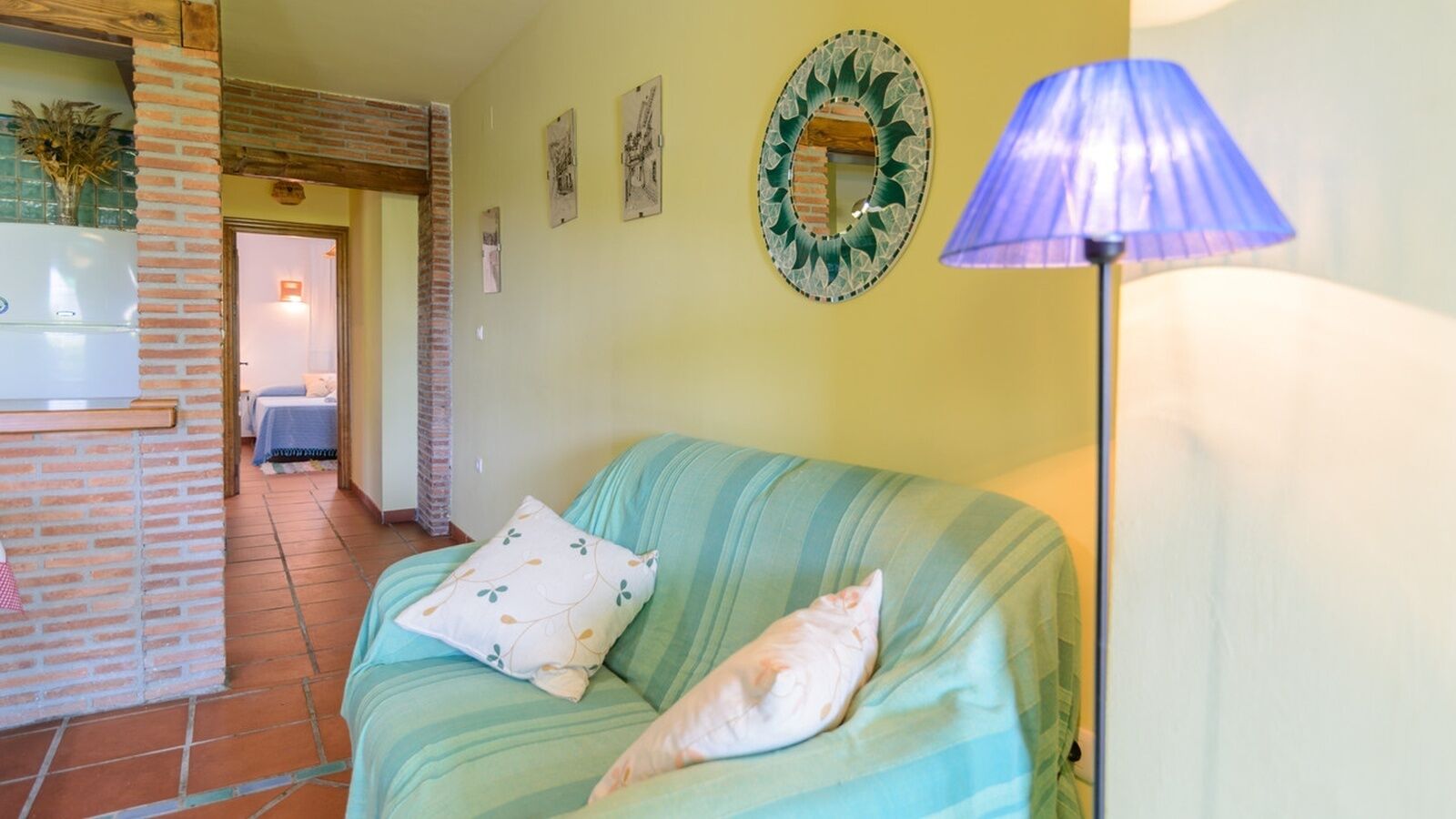 A room with a green sofa, a blue lamp, and a decorative mirror on the wall.