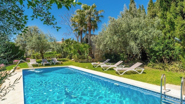 Una piscina rectangular con agua azul cristalina, rodeada por un césped con varias tumbonas.