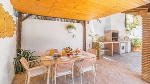 Un área de comedor al aire libre con sillas de mimbre, una mesa dispuesta para el desayuno y un horno de ladrillo.