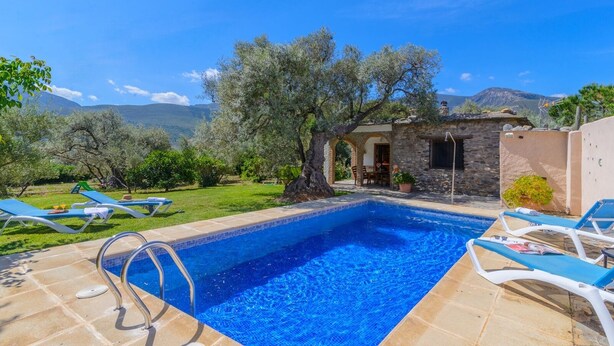 A swimming pool with lounge chairs, a stone building, and a view of mountains. - Cortijo Las Pitas Órgiva by Ruralidays (Granada)