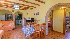 A cozy dining area with a table set for four, surrounded by wooden chairs. A brick fireplace and a kitchen with a tiled backsplash are visible in the background. - Cortijo Las Pitas Órgiva by Ruralidays (Granada)