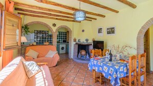 A cozy living area with a sofa, a dining table with a blue tablecloth, a fireplace, and a kitchen area with a washing machine. - Cortijo Las Pitas Órgiva by Ruralidays (Granada)