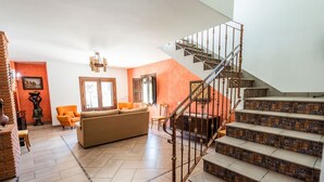 A living room with a sofa, orange armchairs, a staircase with patterned steps, and a chandelier.