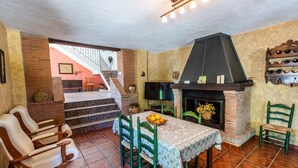 A cozy dining area with a fireplace, a staircase leading to an upper level, and a table set with fruit.