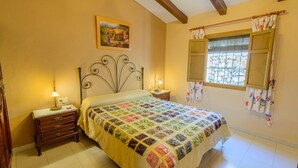 Une chambre à coucher avec un lit, deux tables de chevet, une commode, une fenêtre avec des rideaux et un tableau au mur.