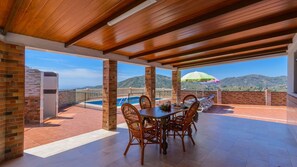 A covered patio with a pool, wooden furniture, and a view of mountains. - Cortijo Metomela Torrox by Ruralidays (Málaga)