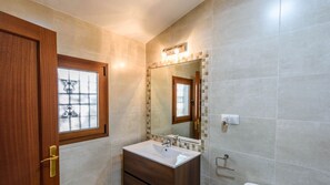 A bathroom with a wooden door, a window, a sink, a mirror, and tiled walls. - Cortijo Metomela Torrox by Ruralidays (Málaga)