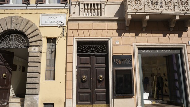 Un bâtiment doté d’une grande porte richement décorée, portant l’inscription « Piazza di Spagna », et d’une boutique nommée « Giuseppe Zanotti », avec des vitrines en verre.
