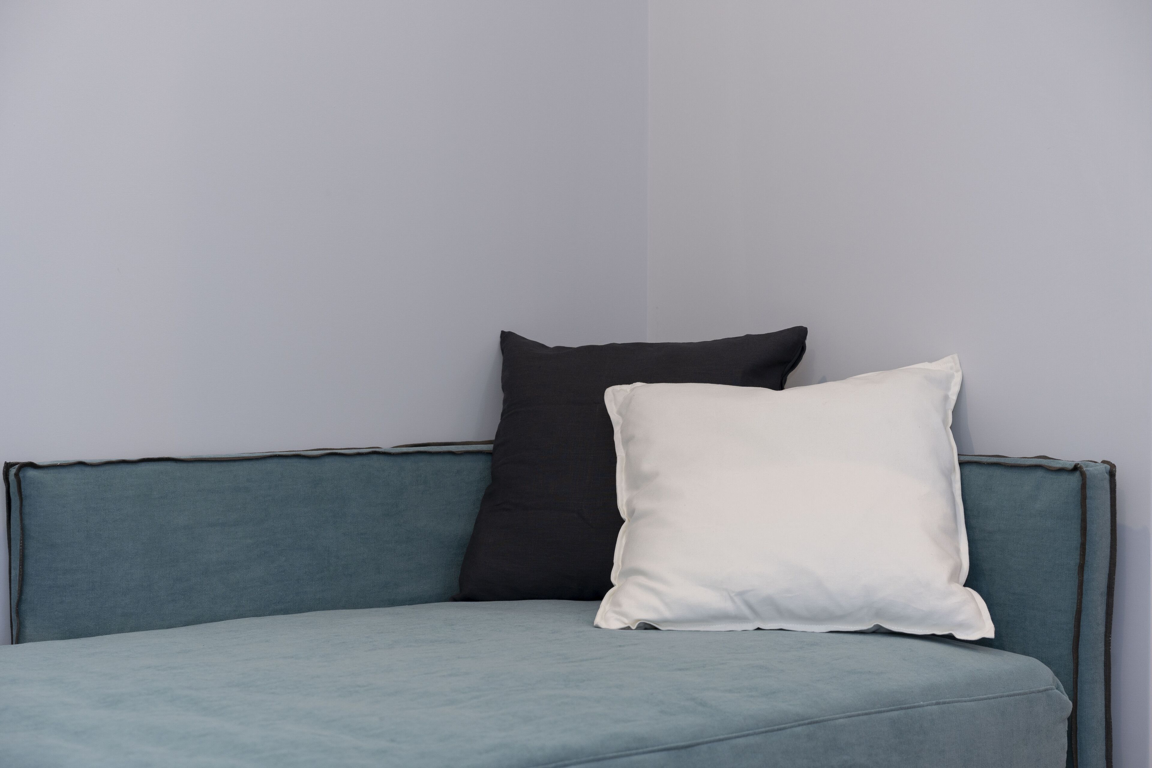 Un canapé bleu clair agrémenté de deux coussins, l’un noir et l’autre blanc, placé devant un mur uni.